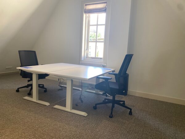 Twee bureaustoelen en een wit tweepersoonsbureau in een licht kantoor aan de Kleine Houtweg.